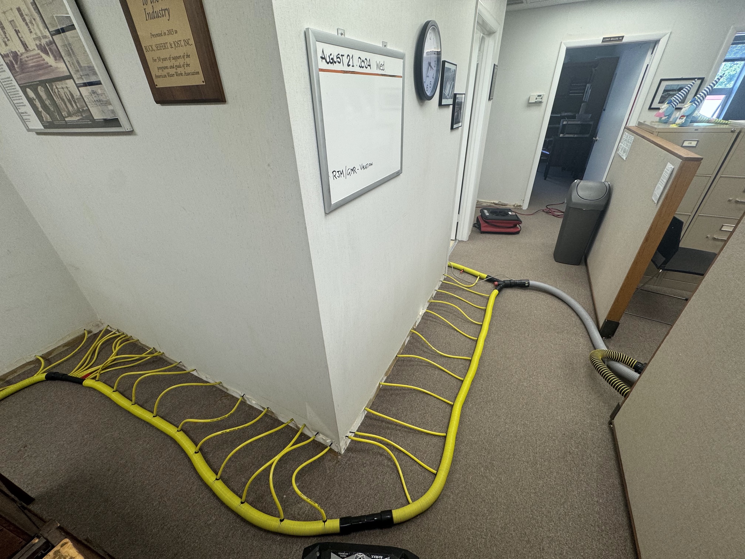 Wall-injection drying equipment installed along baseboards in a commercial office hallway after water damage