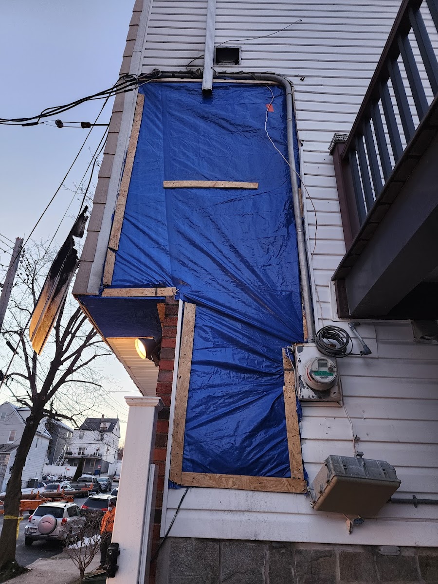 Emergency blue tarp secured over storm-damaged siding on a residential building in the Tri-State area